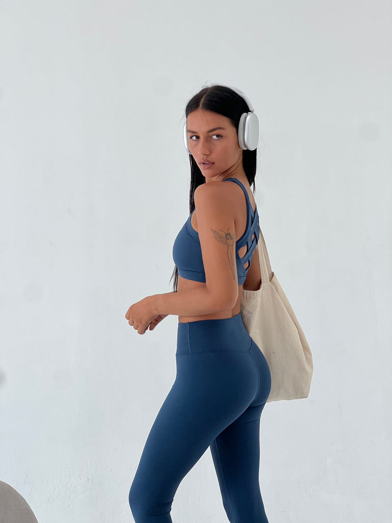 Side angle image of a person wearing the Vitality bra & matching leggings in dusk color & headphones, carrying a tote.